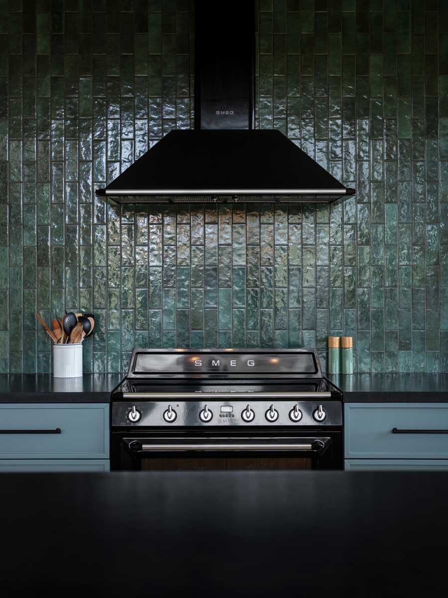 Detail černého sporáku SMEG umístěného před lesklým zeleným keramickým obkladem.