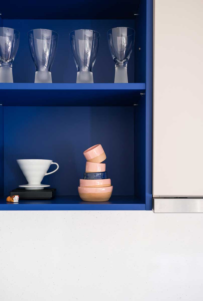 Modrá kuchyňská police s dekorativním sklem, keramickými miskami a minimalistickým kávovým vybavením.