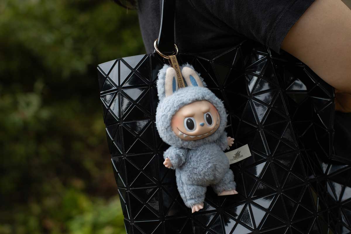 Přívěsek Labubu zavěšený na elegantní černé kabelce s geometrickým vzorem.