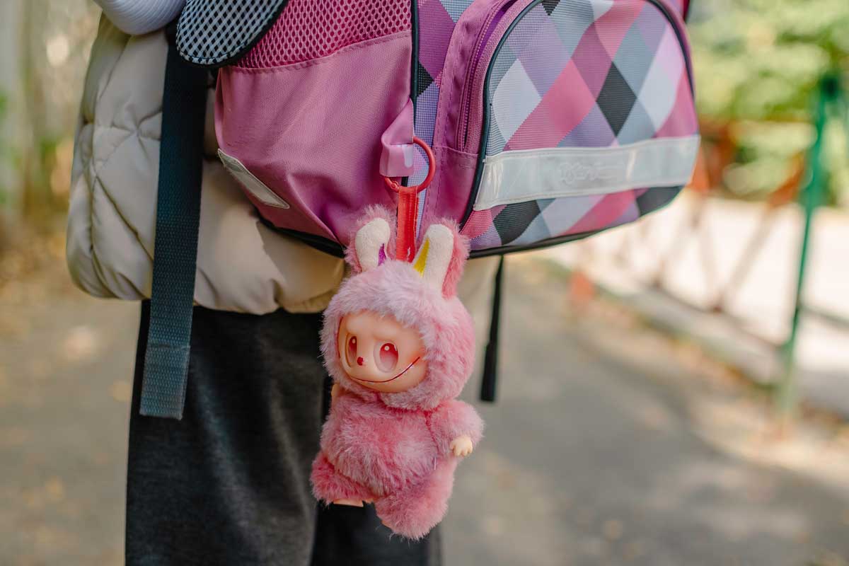 Přívěsek růžového Labubu na školním batohu dítěte během venkovní procházky.