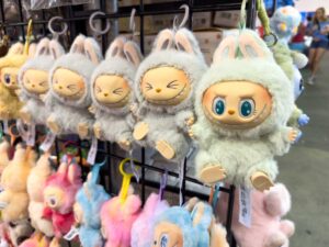 Řada plyšových přívěsků Labubu ve tvaru malých příšerek zavěšených na stojanu.