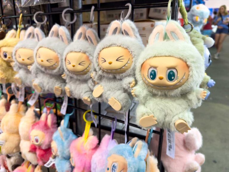 Řada plyšových přívěsků Labubu ve tvaru malých příšerek zavěšených na stojanu.