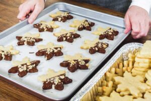 Pečicí plech s hvězdičkami máčenými v čokoládě a posypanými ořechy, připravenými k tuhnutí.