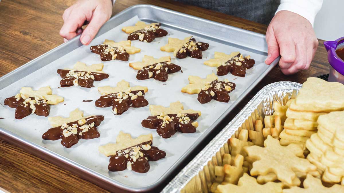 Pečicí plech s hvězdičkami máčenými v čokoládě a posypanými ořechy, připravenými k tuhnutí.