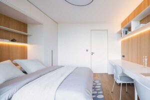 Světlá ložnice s vestavěnými úložnými prostory, dřevěnými akcenty a ambientním LED osvětlením.