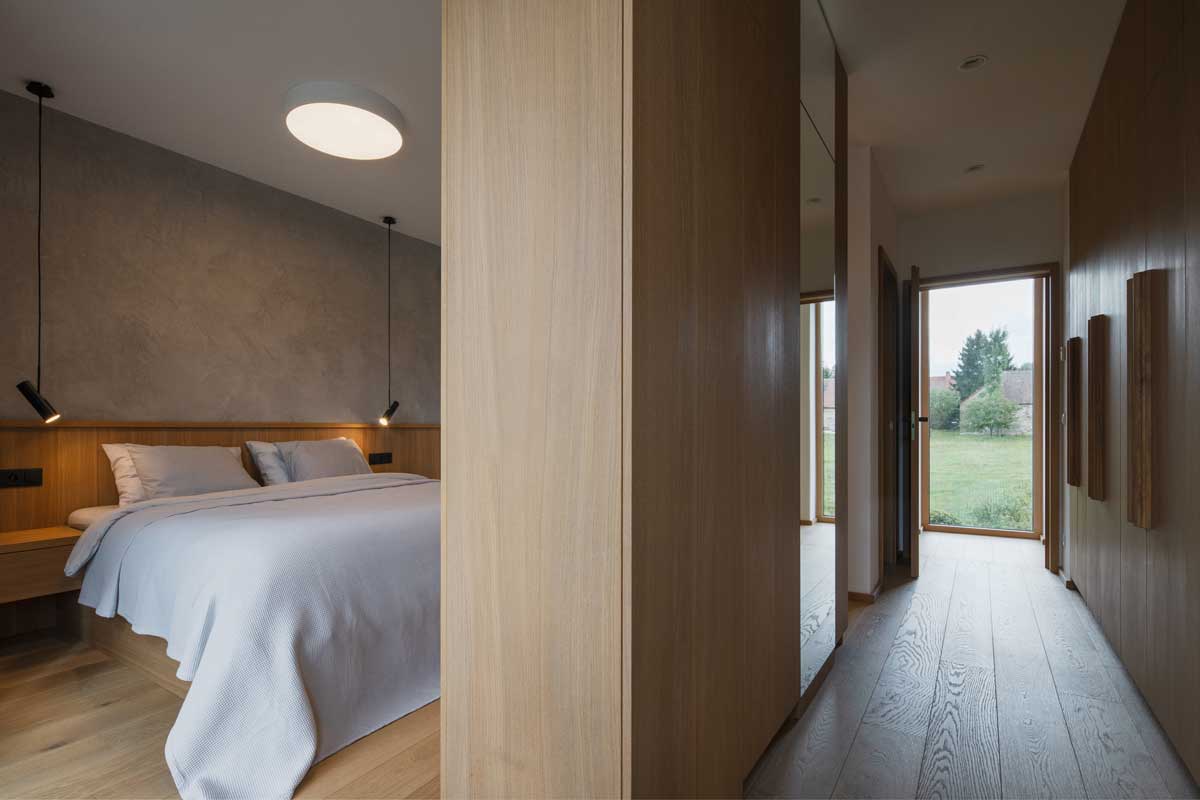 Minimalistická ložnice s dubovou podlahou vestavěným nábytkem a jemným osvětlením.