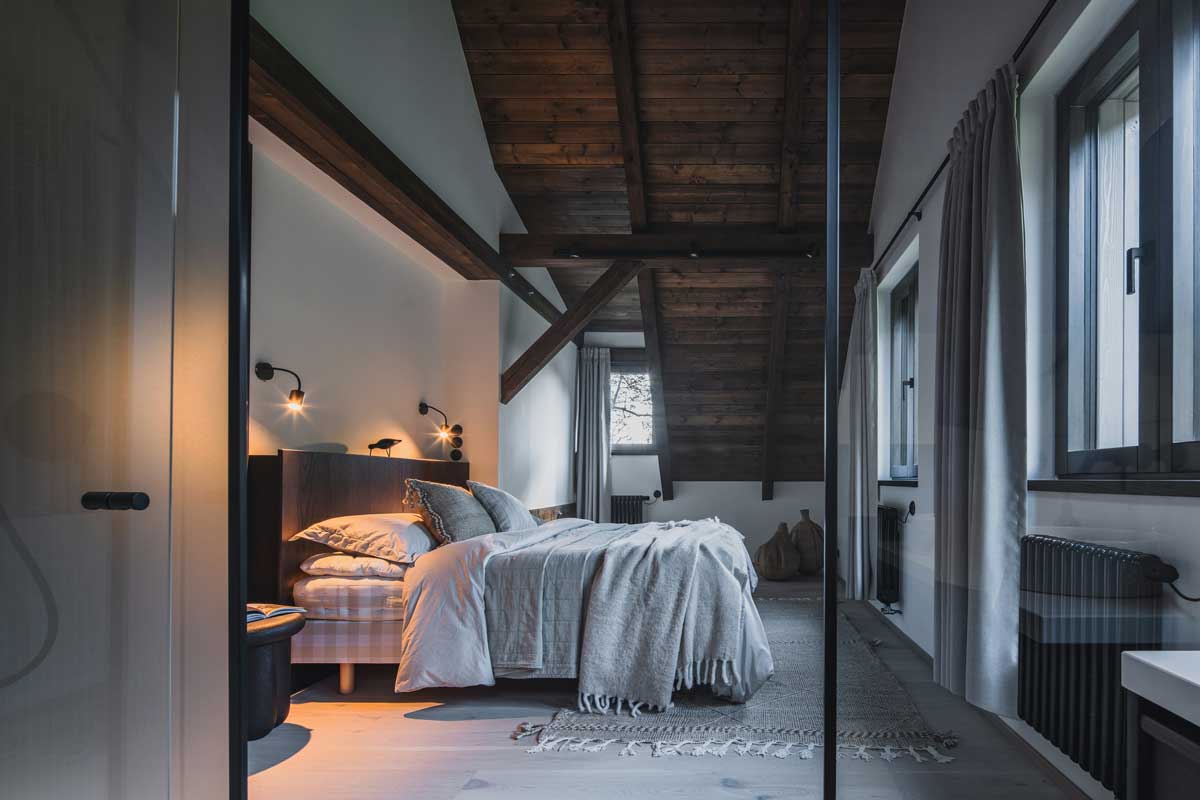 Ložnice v podkroví s odkrytými trámy, jemnými textiliemi a tlumeným světlem