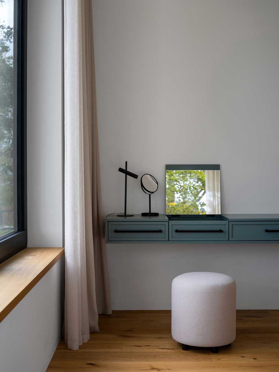 Minimalistický toaletní koutek s designovými zrcadly a pudrovým taburetem v moderní ložnici.