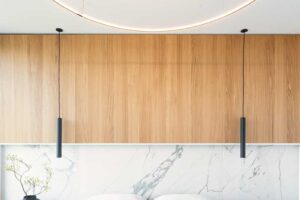 Designová ložnice s mramorovým obkladem za čelem postele, dýhovaným panelem a závěsnými černými svítidly.