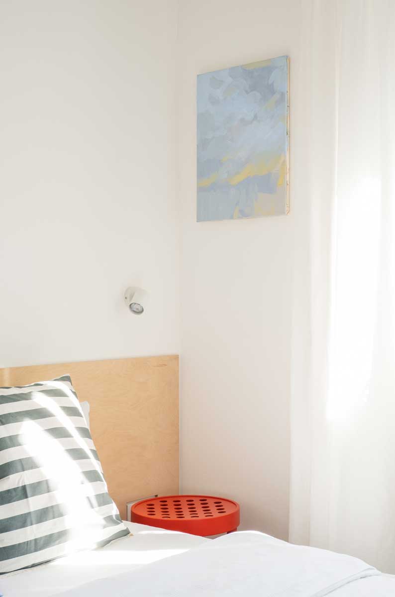 Světlá ložnice s minimalistickou kompozicí, obrazem v modrých tónech a dřevěnou postelí.