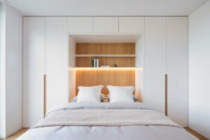 Světlá ložnice s integrovaným nábytkem, dřevěným obkladem a ambientním LED páskem