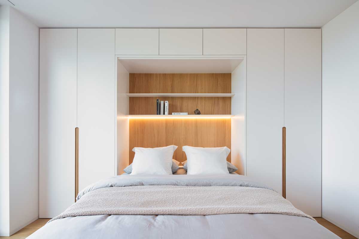 Světlá ložnice s integrovaným nábytkem, dřevěným obkladem a ambientním LED páskem