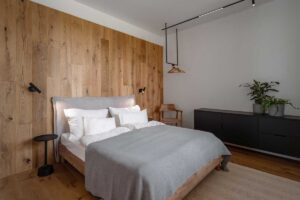 Moderní ložnice s dřevěným obkladem, útulným lůžkem a tlumenou paletou textilií.