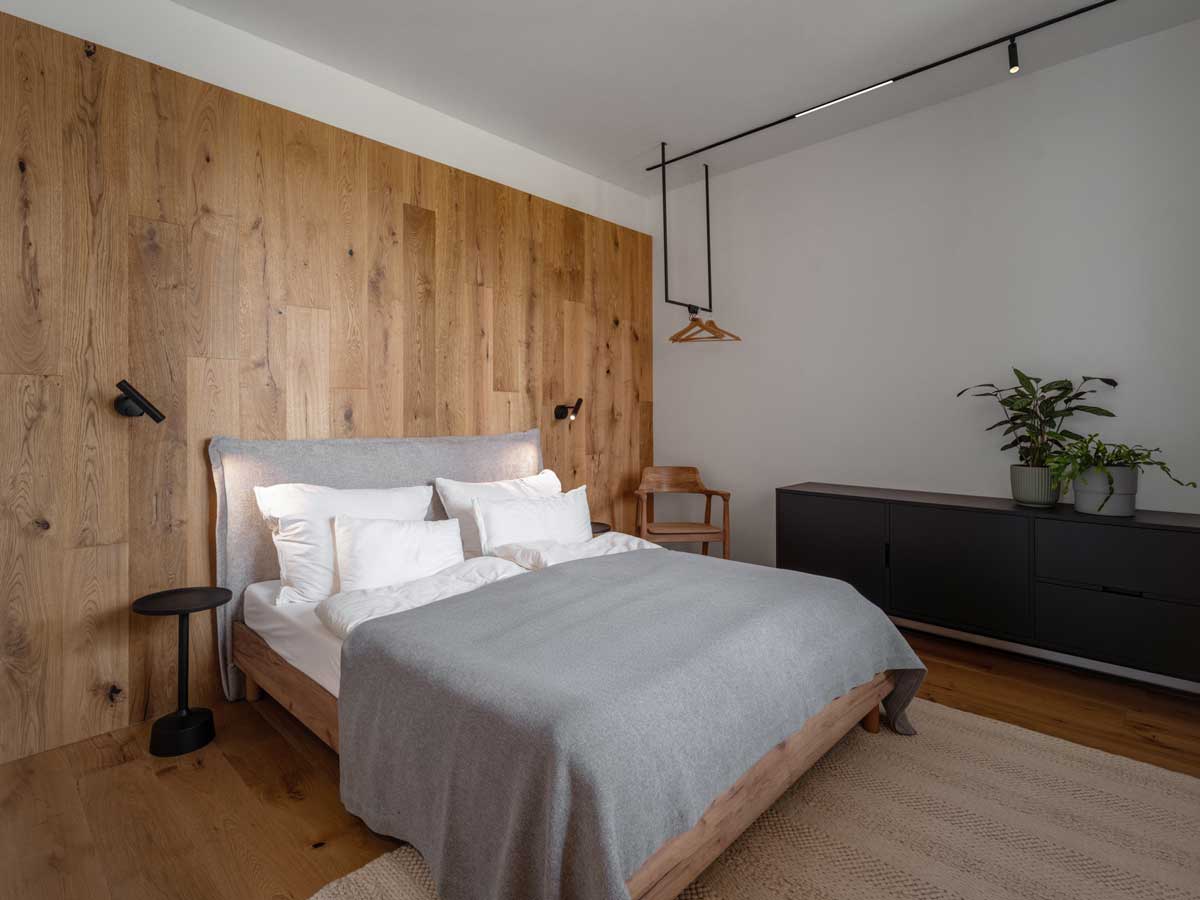 Moderní ložnice s dřevěným obkladem, útulným lůžkem a tlumenou paletou textilií.