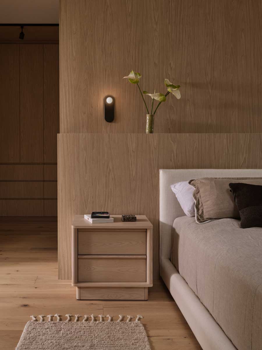 Ložnice s čalouněnou postelí, dřevěným nočním stolkem a jemným osvětlením