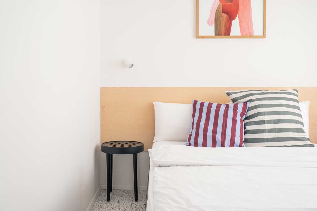 Minimalistický černý noční stolek vedle světlého čela postele.