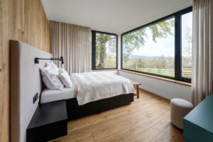 Světlá ložnice s panoramatickým oknem a výhledem do krajiny.