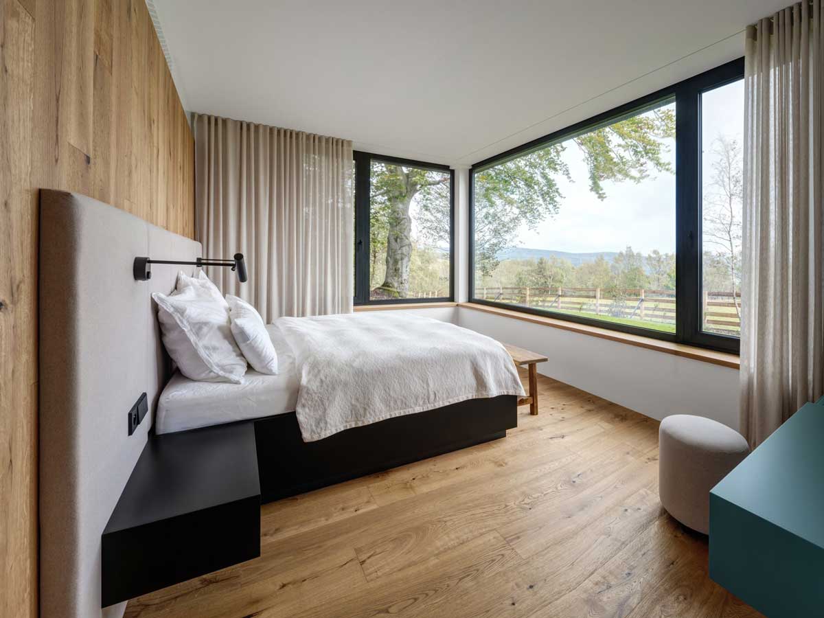 Světlá ložnice s panoramatickým oknem a výhledem do krajiny.