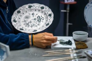 Ruční malování porcelánu modrým kobaltovým pigmentem na talíř, detail práce řemeslníka při tvorbě tradičního dekoru