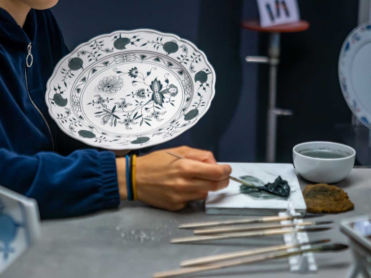 Ruční malování porcelánu modrým kobaltovým pigmentem na talíř, detail práce řemeslníka při tvorbě tradičního dekoru