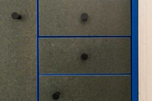 Detail koupelnové skříňky s modrým rámem a tmavými dvířky z recyklovaného materiálu.