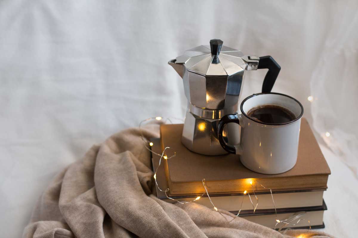 Moka konvička s hrnkem položená na knihách vytváří klidnou scenérii ideální pro pomalá rána