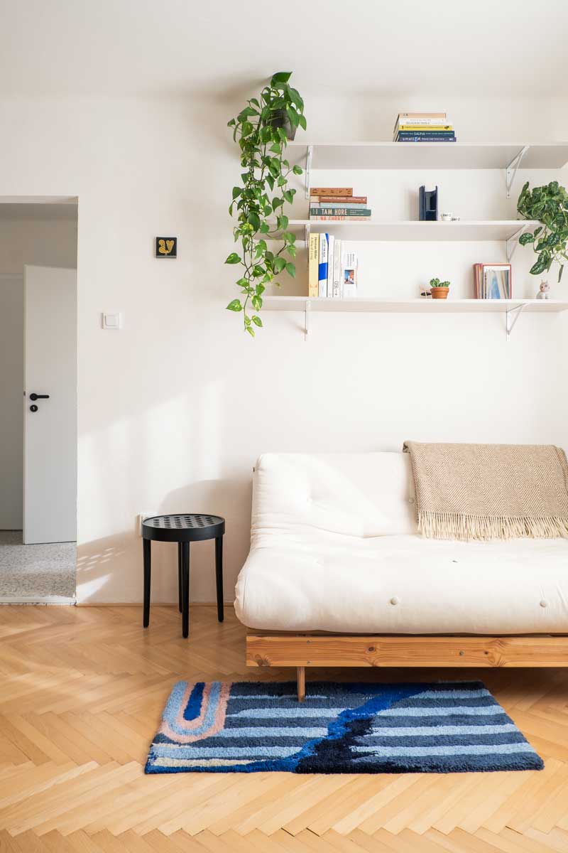 Obývací pokoj s nízkou pohovkou, kobercem a minimalistickými policemi s knihami.