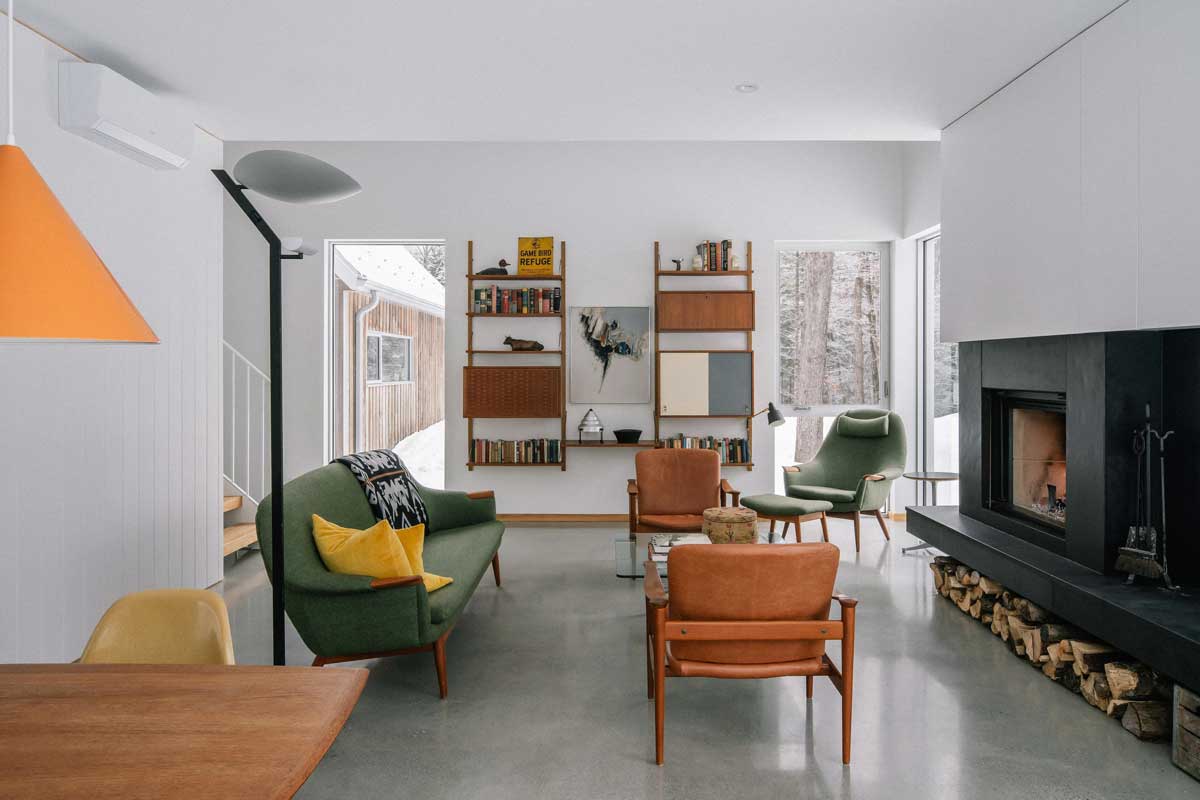 Obývací pokoj s mid century nábytkem a velkými okny nabízí výhled do zasněženého lesa.