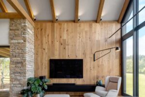 Moderní obývací pokoj s vysokým stropem, dřevěnou stěnou a velkými prosklenými plochami.