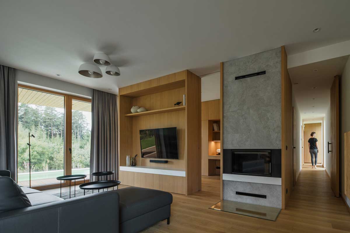 Obývací pokoj s krbem dubovým nábytkem a velkými prosklenými plochami směrem do zahrady.