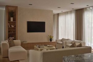 Obývací pokoj s vestavěným nábytkem, světlými sedačkami a velkými okny se záclonami