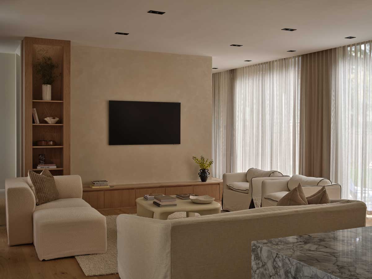 Obývací pokoj s vestavěným nábytkem, světlými sedačkami a velkými okny se záclonami