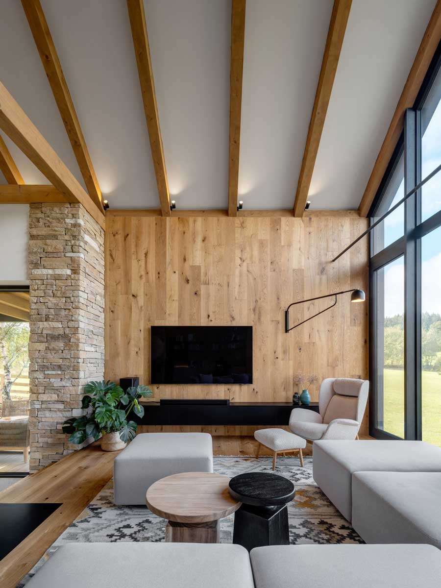 Moderní obývací pokoj s vysokým stropem, dřevěnou stěnou a velkými prosklenými plochami.