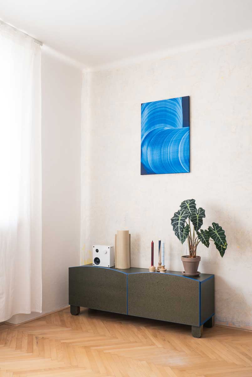 Designová TV skříňka s modrými detaily a výrazným abstraktním obrazem nad ní.