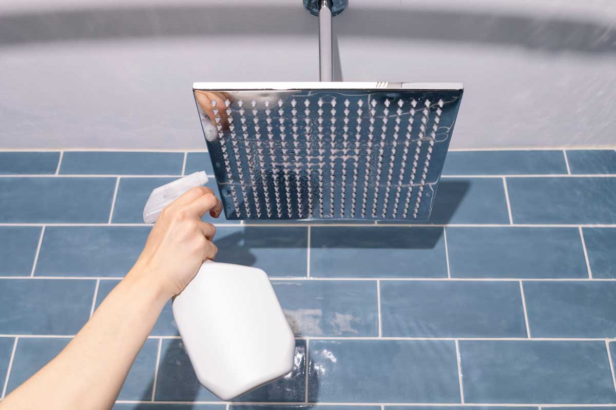 Ruka nanášející octový postřik na sprchovou hlavici jako prevenci proti zimnímu usazování vodního kamene.