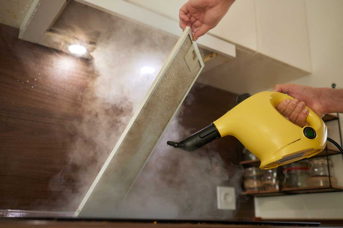 Čištění zaneseného filtru digestoře pomocí parního čističe pro snadné odstranění mastnoty