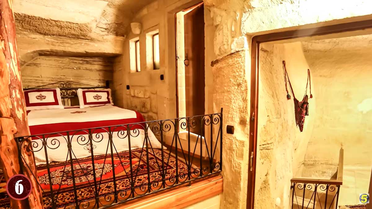 Luxusní ložnice v podzemním domě s ručně tesanými kamennými stěnami a kovovým zábradlím