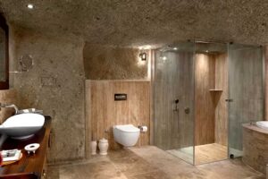 Prostorná moderní koupelna vybudovaná v podzemí s kamennými stěnami a skleněným sprchovým koutem