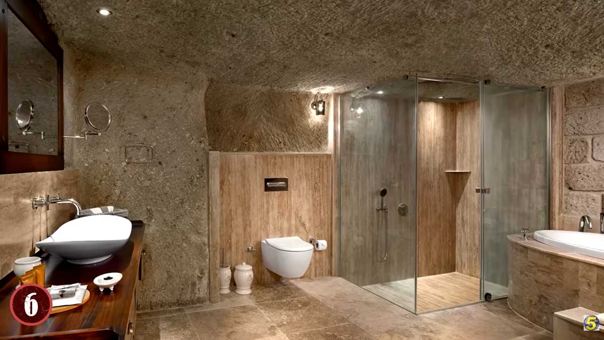 Prostorná moderní koupelna vybudovaná v podzemí s kamennými stěnami a skleněným sprchovým koutem