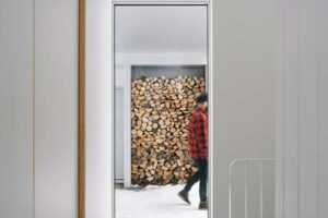 Průhled chodbou odhaluje venkovní zásobu dřeva a propojuje interiér s tichou zimní krajinou.