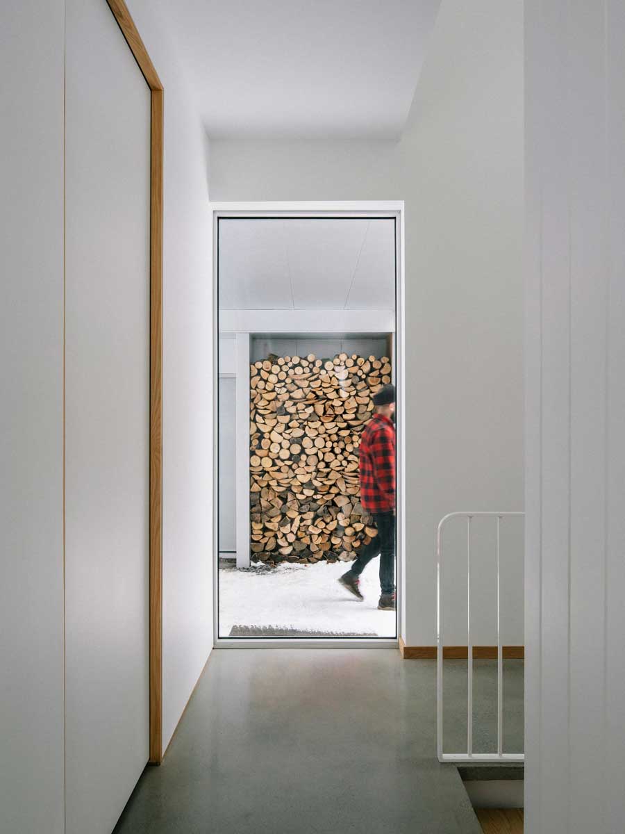 Průhled chodbou odhaluje venkovní zásobu dřeva a propojuje interiér s tichou zimní krajinou.
