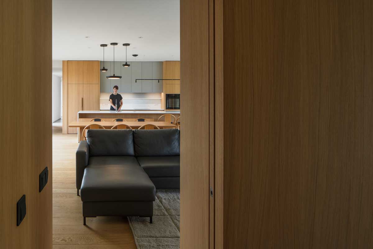 Průhled z chodby do otevřené denní zóny s kuchyní a obývacím prostorem.