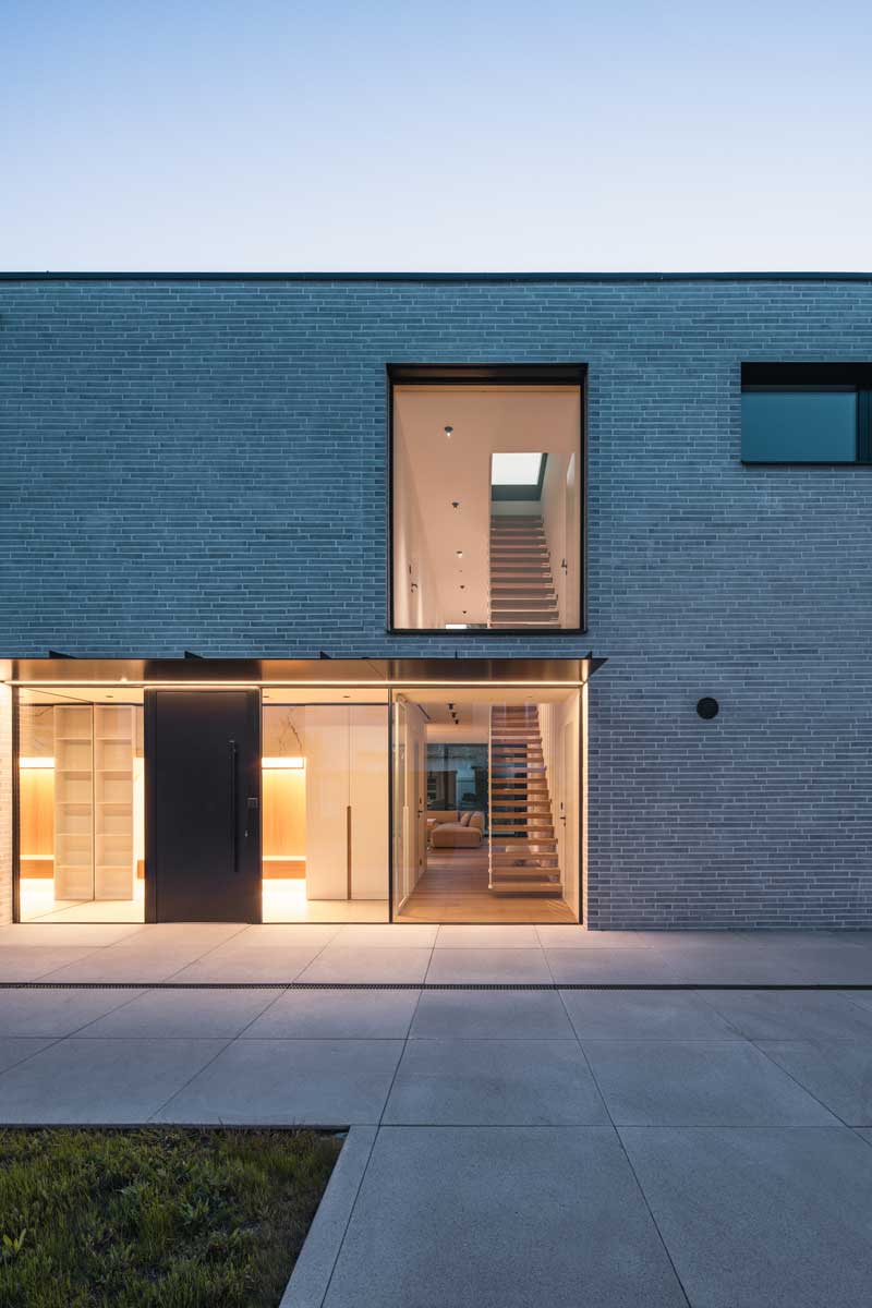 Prosklený vstup rodinného domu s pohledem na plovoucí schodiště a minimalistický interiér