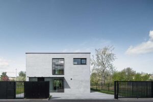 Moderní rodinný dům z bílo-šedé cihly s černými rámy oken a minimalistickou vstupní částí