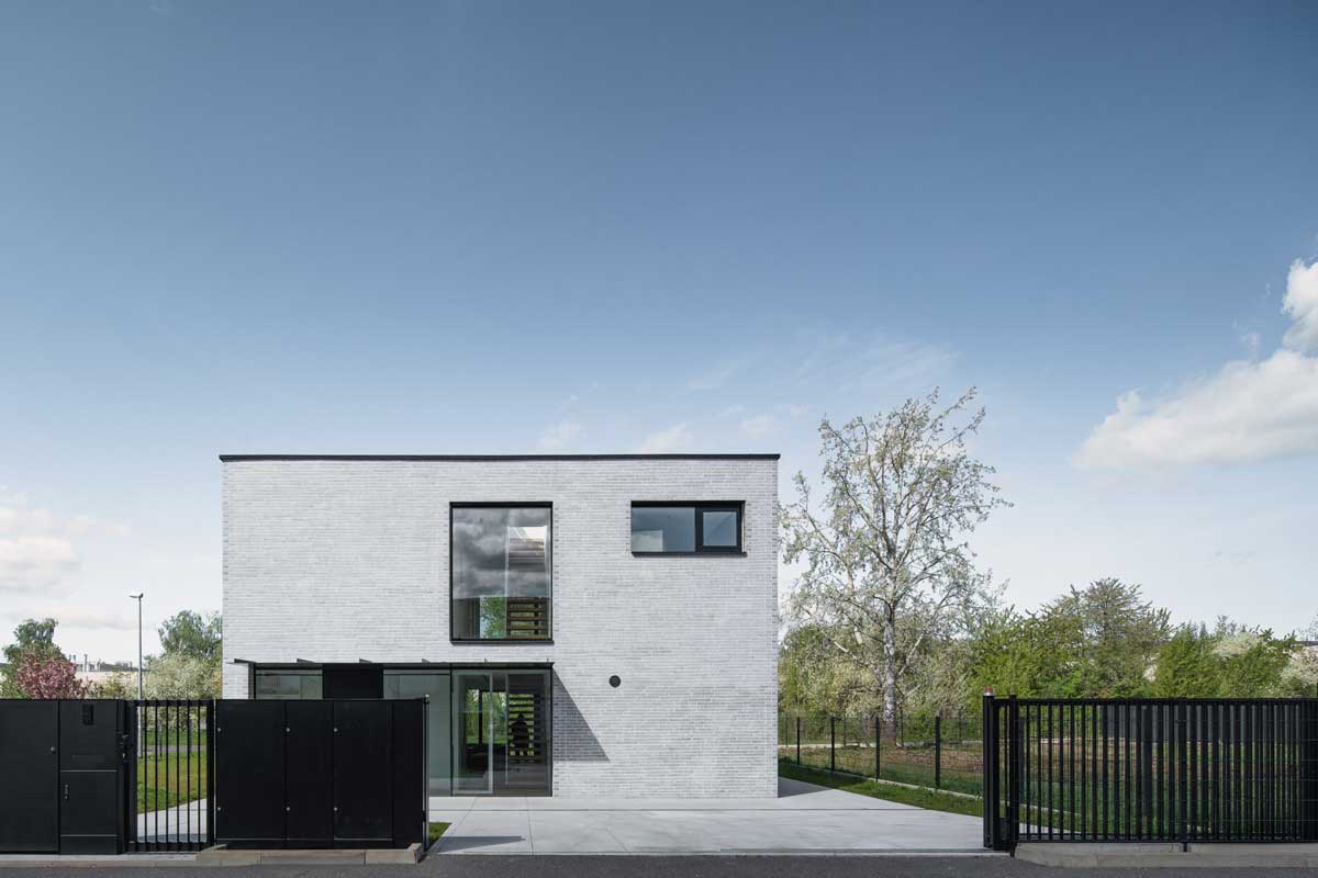 Moderní rodinný dům z bílo-šedé cihly s černými rámy oken a minimalistickou vstupní částí