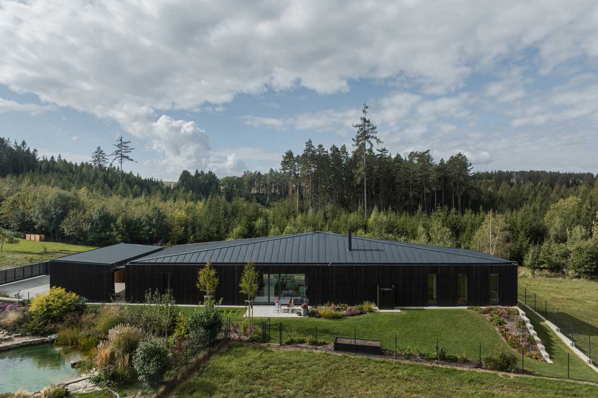 Letecký pohled na minimalistický rodinný dům s rozlehlou zahradou v přírodní krajině Vysočiny.