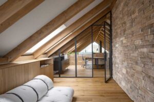 Podkrovní odpočinkový kout s futonem a výhledem do pracovny v moderní horské chatě.