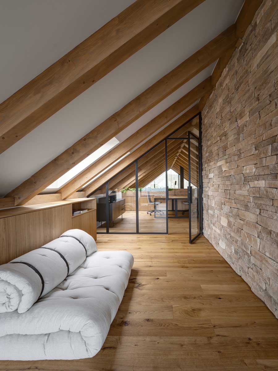 Podkrovní odpočinkový kout s futonem a výhledem do pracovny v moderní horské chatě.