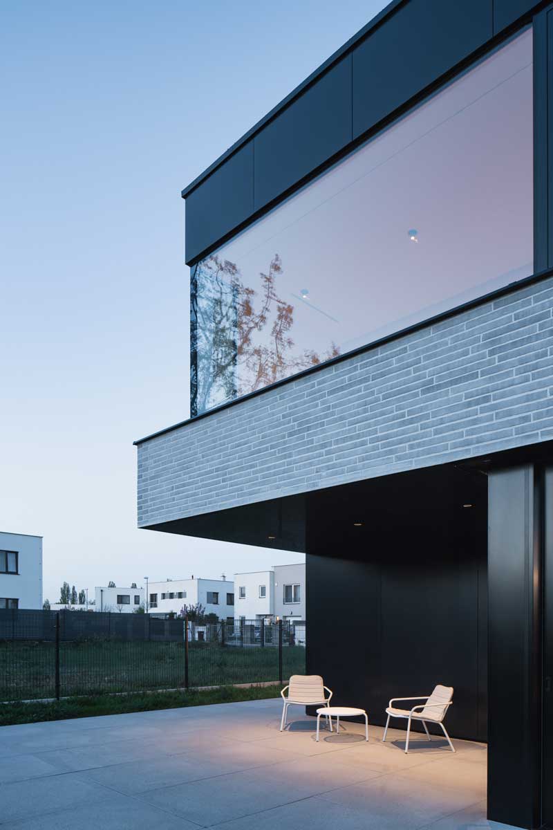 Minimalistická terasa s dvěma zahradními křesly pod přesahem patra