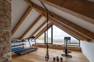 Domácí posilovna v podkroví s dřevěnou podlahou a výhledem na okolní krajinu.
